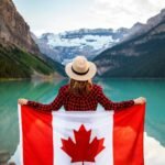 Woman holding a Canadian flag at stunning Lake Louise, Alberta, embracing nature and patriotism.