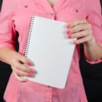 A woman in a pink shirt holds a blank notepad, ideal for mockup use.