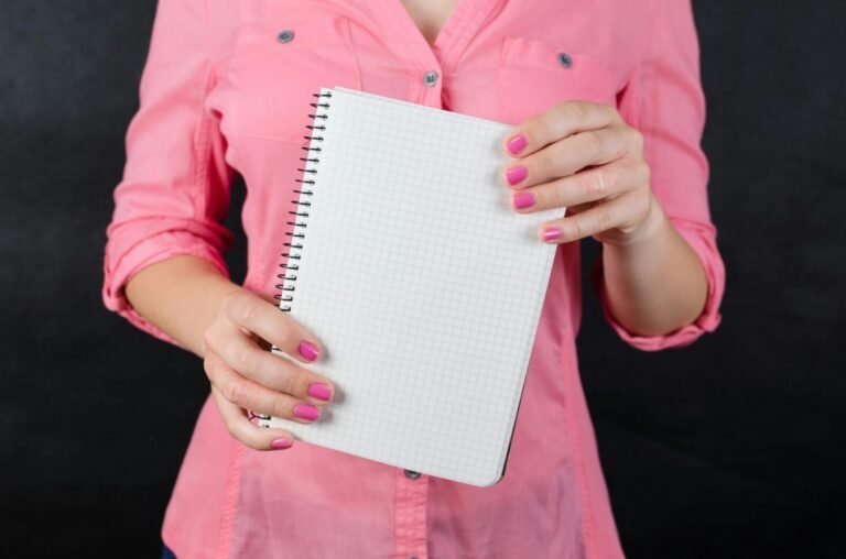 A woman in a pink shirt holds a blank notepad, ideal for mockup use.